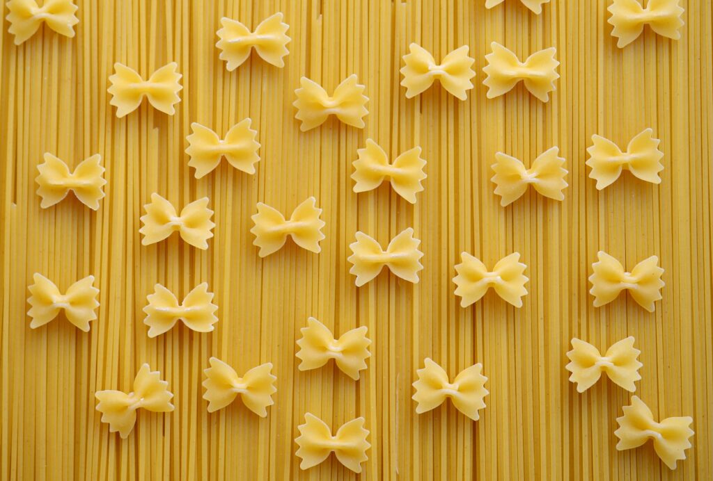 Flat lay of Italian pasta varieties, showcasing farfalle and spaghetti on a neutral background.